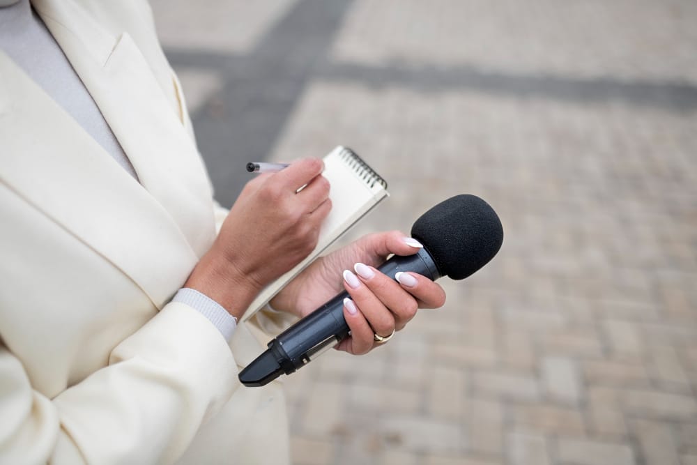 femme tenant un micro dans la main gauche et un petit carnet de notes et un stylo dans la main droite